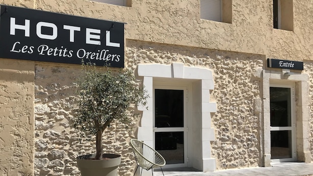 A hotel named "HOTEL Les Petits Oreillers" with a stone facade, a potted tree, and a chair outside. - Hôtel Les Petits Oreillers (Saint-Martin-d'Ardèche)