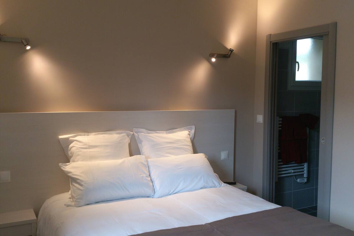 Una cama bien tendida con sábanas blancas en una habitación de diseño sencillo y limpio.