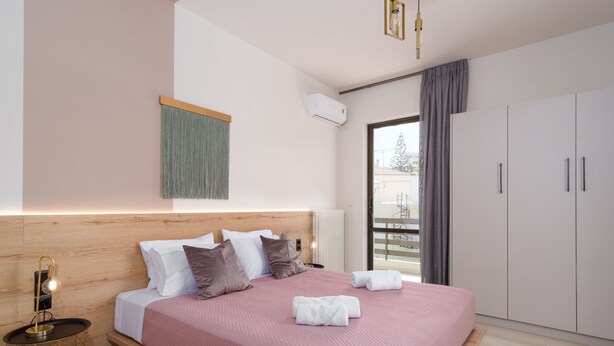 Un dormitorio moderno con cabecera de madera, una cama grande con ropa de cama rosa y un armario.