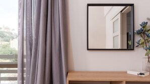 Una habitación con un ventanal grande, un espejo, una consola de madera, un otoman rosa y una alfombra con motivos geométricos.