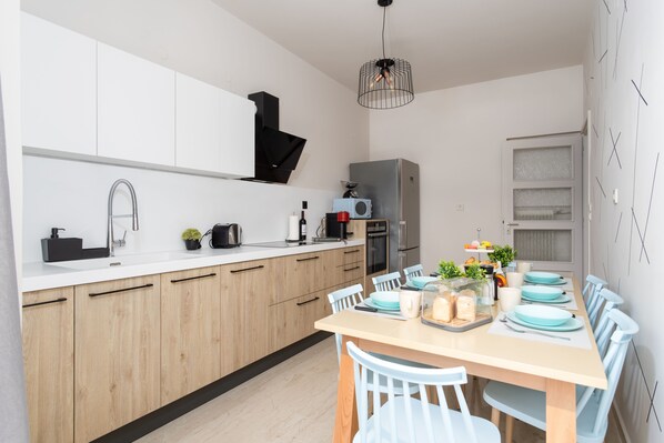 Une cuisine moderne avec des meubles en bois, un plan de travail blanc et un coin repas avec une table dressée pour quatre personnes.