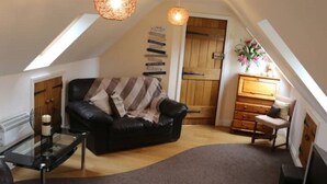 Ein gemütliches Schlafzimmer im Loft-Stil mit gewölbter Decke, einer schwarzen Ledersofa, einem Glastisch, einer Holzkommode und einem großen Fenster mit Blick ins Freie.