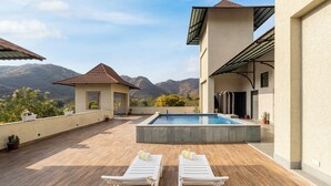 A rooftop pool area with two lounge chairs, a small pool, and a view of mountains. - The Hunting Lodge (Udaipur)