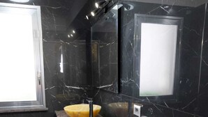 Un bany modern amb parets de marbre negre, un tocador de fusta i un lavabo groc.