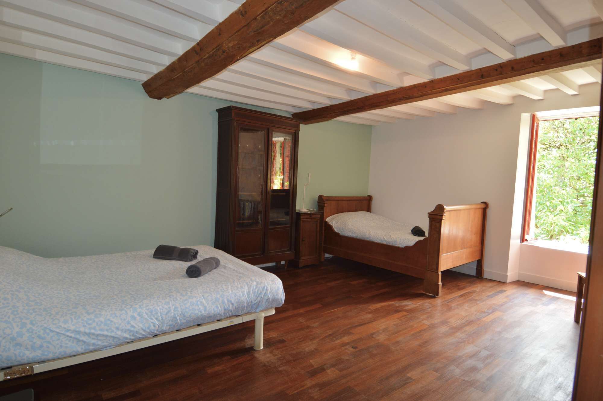 Un dormitorio con dos camas de madera, un armario y una ventana con vistas a zonas verdes.