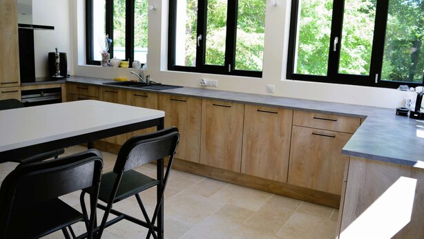 A modern kitchen with a large window, wooden cabinets, and a dining area with chairs.