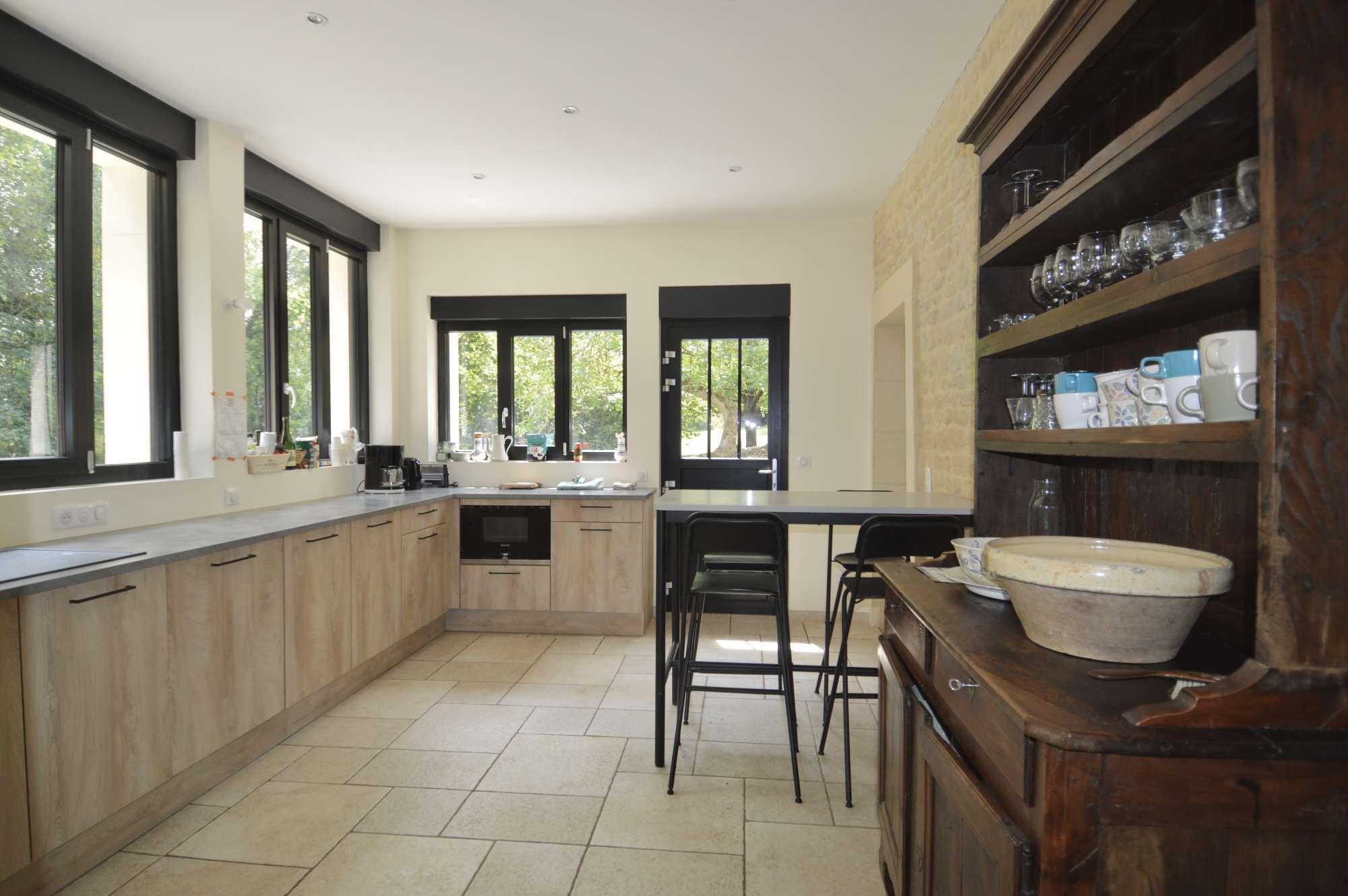 Una cuina moderna amb grans finestres, una illa central i un armari de fusta amb vidrieria.