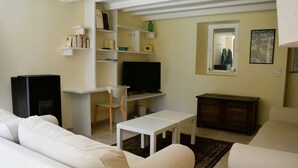 A living room with a white sofa, a white table, a TV, and a bookshelf.