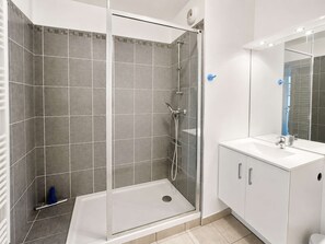 A modern bathroom with a glass-enclosed shower, a white sink, and a mirror. - Spacious apartment - Balcony - 50m from the beach (Courseulles-sur-Mer)