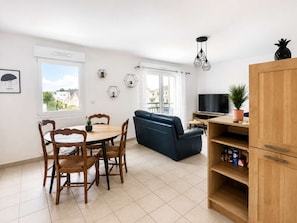 A modern living room with a sofa, a dining table with chairs, a TV, and a wooden cabinet. - Spacious apartment – balcony – 50 m from the beach (Courseulles-sur-Mer)