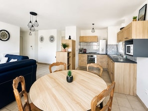 A modern kitchen with wooden cabinets, a dining table, and a blue sofa in the living area.