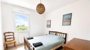 Une chambre à coucher comprenant un lit, une chaise, une table de chevet, un luminaire suspendu et deux tableaux encadrés accrochés au mur.