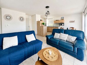 A modern living room with two blue sofas, a coffee table, and a kitchen in the background.