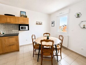 A modern kitchen with wooden cabinets, a built-in microwave, and a dining area with a round table and chairs. - Spacious apartment - Balcony - 50m from the beach (Courseulles-sur-Mer)