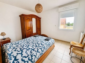 A bedroom with a bed, wooden wardrobe, wicker chair, and a window with a view.