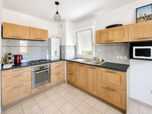 A modern kitchen with wooden cabinets, a gas stove, an oven, a microwave, and a window with blinds.