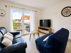 A modern living room with a leather sofa, a blue armchair, a television, and a small table. - Spacious apartment – balcony – 50 m from the beach (Courseulles-sur-Mer)