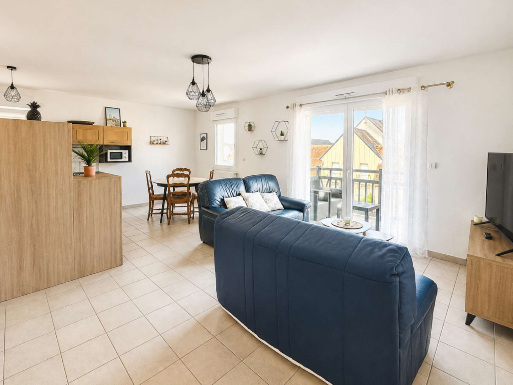 Un salon moderne avec un canapé, un coin repas avec des chaises, une cuisine avec des placards et un balcon doté d’une balustrade.
