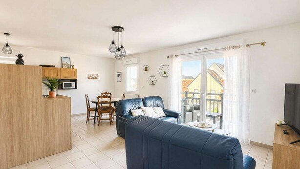 Un salon moderne avec un canapé, un coin repas avec des chaises, une cuisine avec des placards et un balcon doté d’une balustrade.