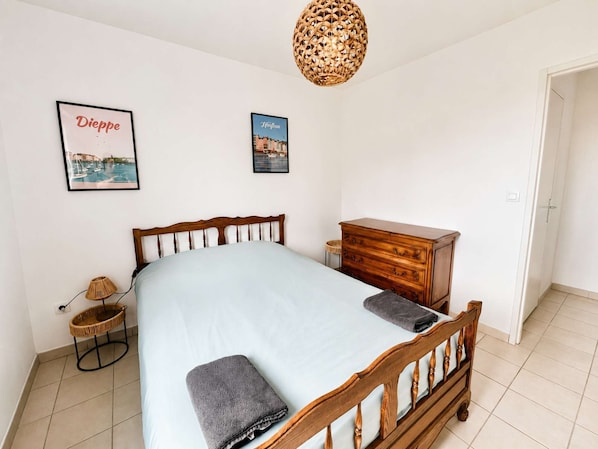 A bedroom with a bed, a dresser, a lamp, and two framed pictures on the wall.