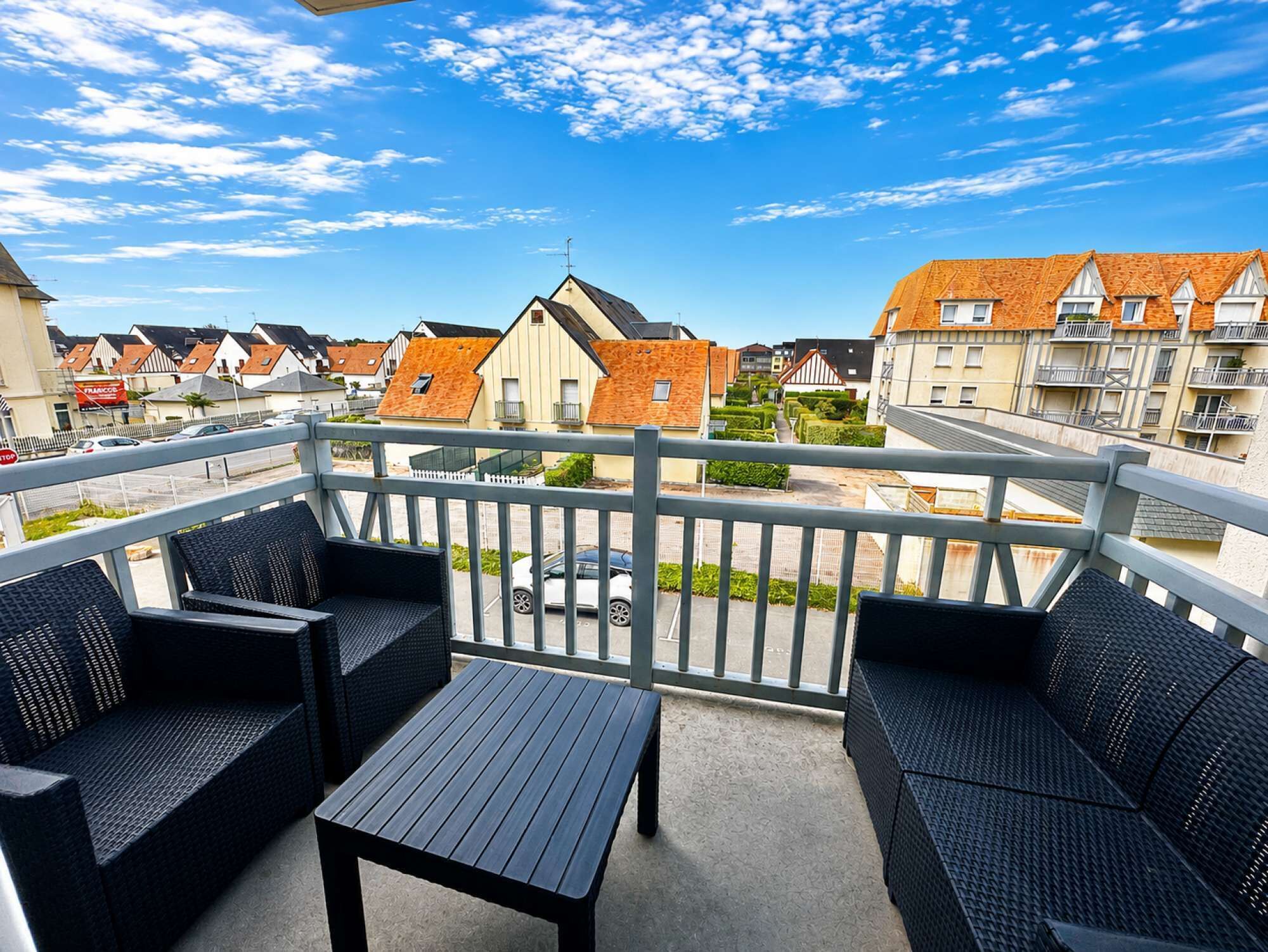 Ein Balkon mit Korbmöbeln, Blick auf Wohnhäuser und einen klaren Himmel.