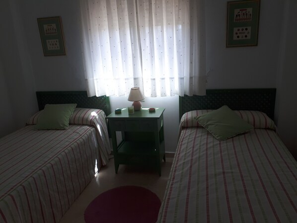 A room with two beds, a small table with a lamp, and a window with curtains.