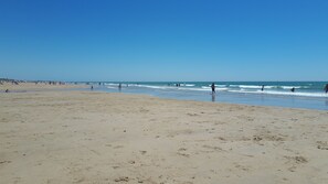 A wide sandy beach with gentle waves and clear skies.