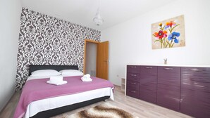 A bedroom with a bed, a wooden door, a purple wardrobe, and a wall with a floral painting. - Villa Bender (Dugopolje)