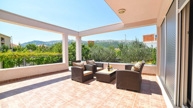 A covered outdoor patio with wicker furniture and a tiled floor, overlooking a mountainous landscape. - Villa Bender (Dugopolje)