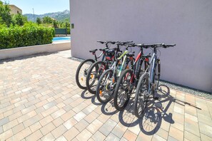 Varias bicicletas están aparcadas contra una pared en un espacio al aire libre con suelo de baldosas.