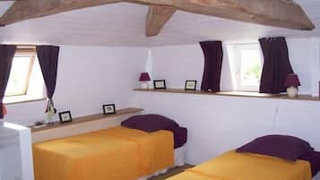 Two single beds with matching bedspreads and pillows, a sloped ceiling with exposed beams, and a cozy reading nook.