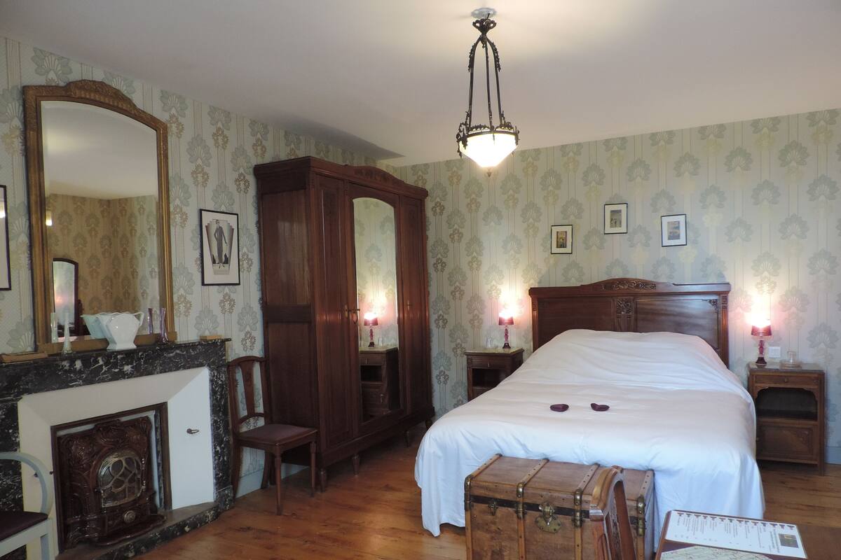 A bedroom with a large bed, a wooden wardrobe, a chest of drawers, a vanity with a mirror, and a chandelier.