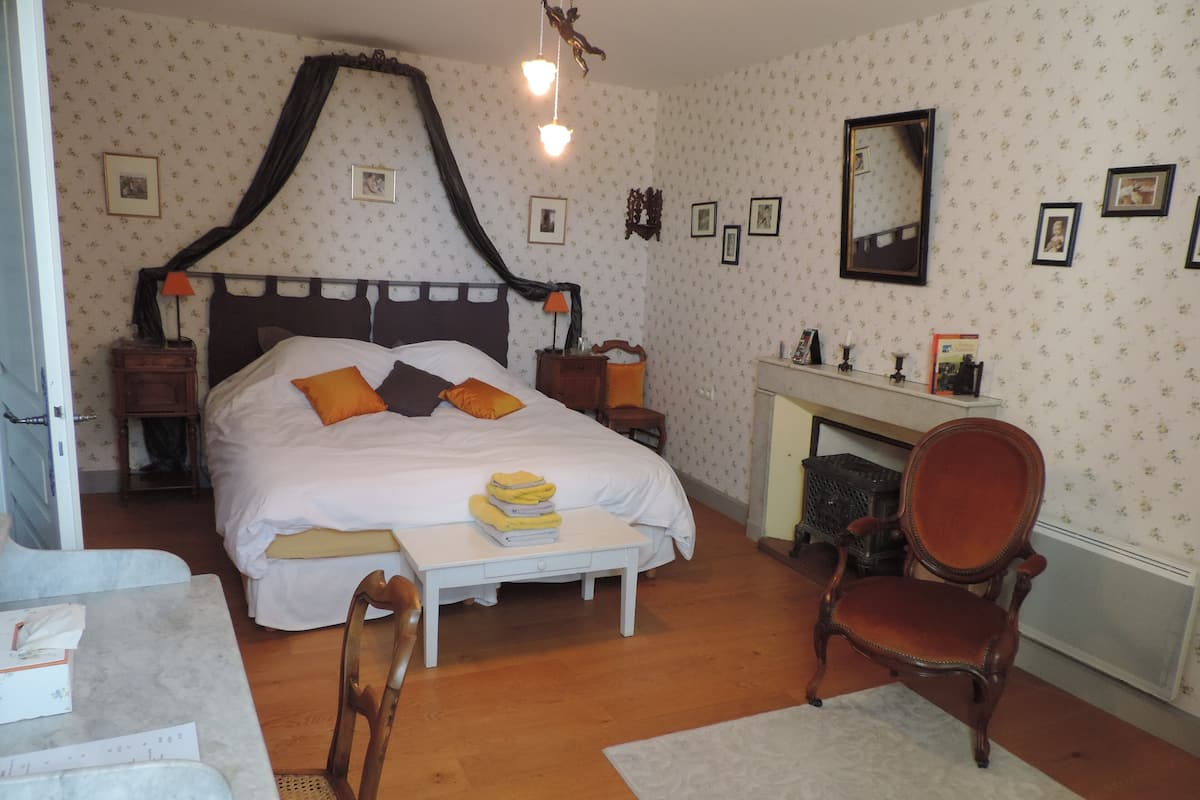 A bedroom with a four-poster bed, a wooden chair, a small table, and a fireplace.