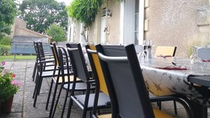 An outdoor patio with tables and chairs, a hanging plant, and a building with a textured wall and windows.