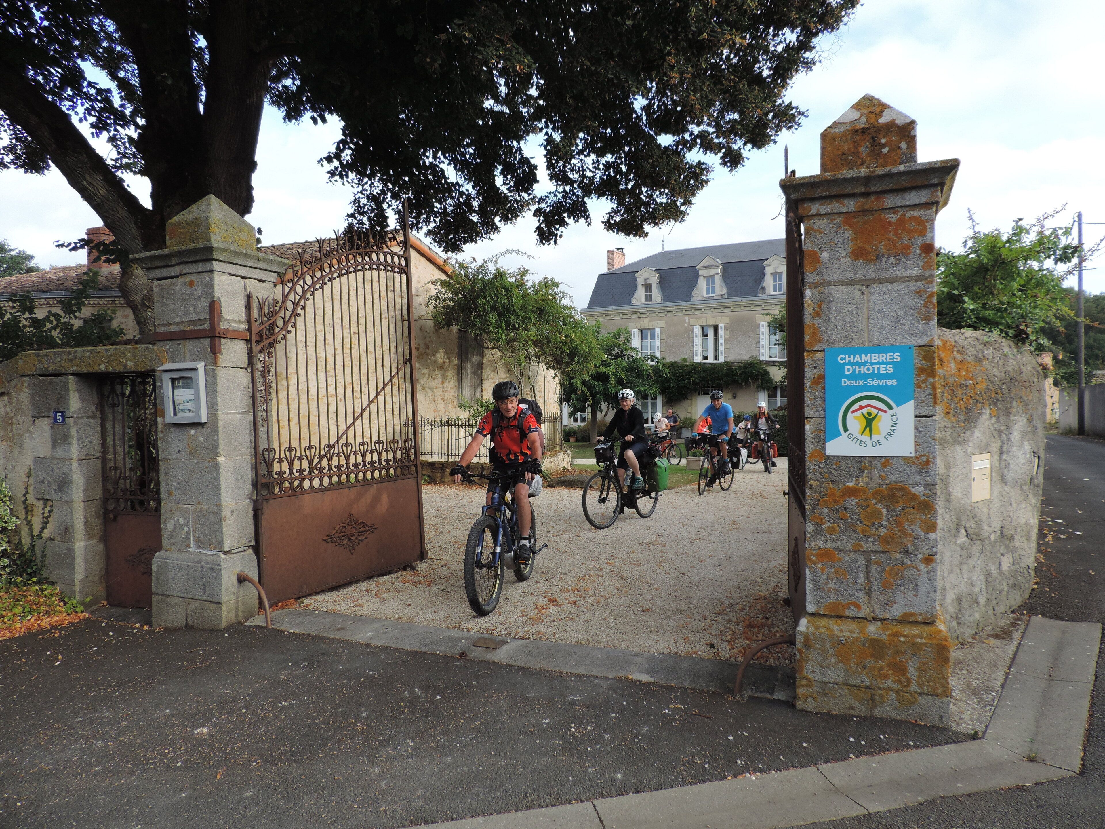 Ein verschlossenes Tor mit einem Schild für Chambres D'Hotes Deux-Sevres, ein historisches Gebäude mit einer Steinfassade und einem großen Baum davor.