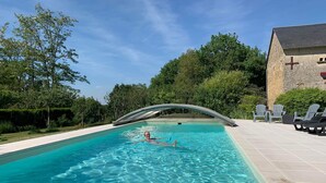 A swimming pool with a glass bridge, surrounded by greenery and a building with a cross on the wall.