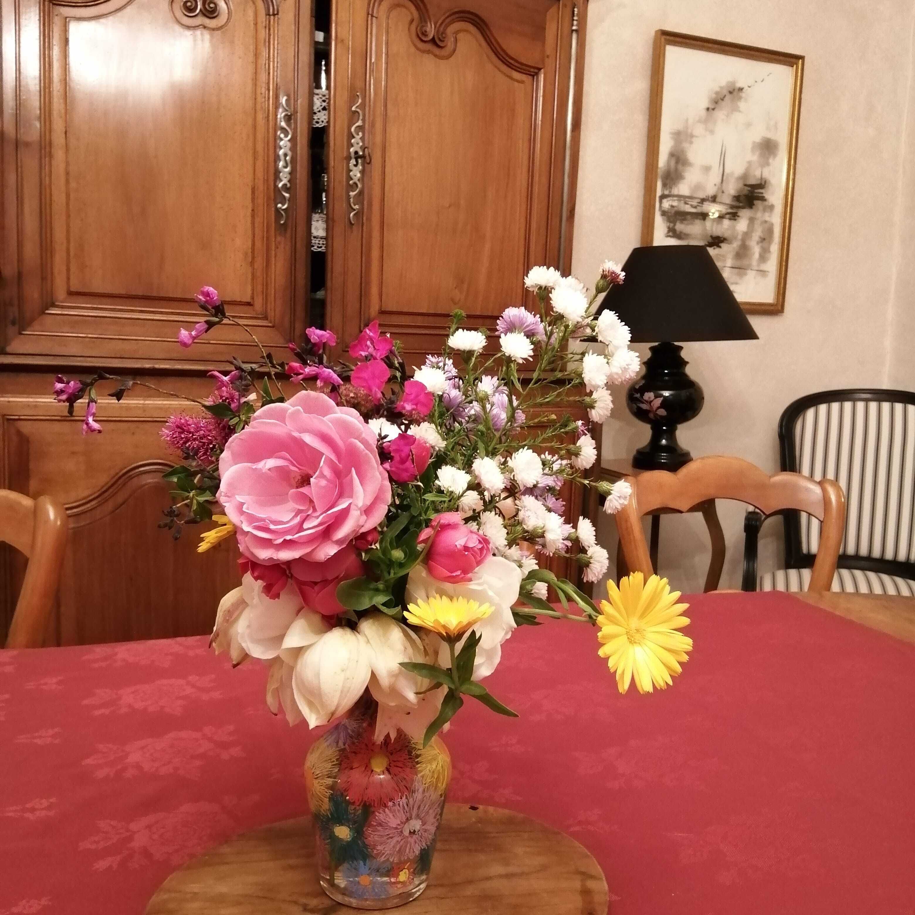 Une table à manger agrémentée d’un centre de table floral dans un vase, des chaises en bois, une lampe et un tableau encadré au mur.