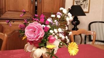 Une table à manger agrémentée d’un centre de table floral dans un vase, des chaises en bois, une lampe et un tableau encadré au mur.