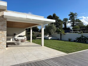 A modern outdoor kitchen area with a stone wall, a wooden ceiling, and a dining set. - LUXURIOUS ARCHITECT-DESIGNED VILLA with an INFINITY POOL and a VIEW OF THE FOREST (Belin-Béliet)