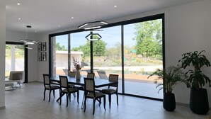 A spacious dining area with a large table and chairs, large windows offering a view of a garden and outdoor play area. - LUXURIOUS ARCHITECT VILLA with OVERFLOW SWIMMING POOL and FOREST VIEW (Belin-Béliet)