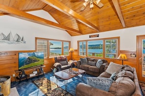 A cozy cabin interior with a large TV, wooden furniture, and a scenic lake view.