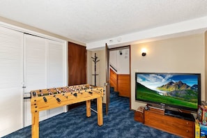Ein Zimmer mit Tischfußball, Fernseher und einer Treppe.