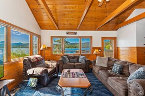 A cabin interior with a wooden ceiling, large windows offering a view of the lake, and a sign reading 'WELCOME TO THE LAKE'.