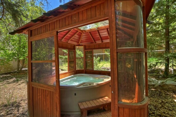 A hot tub structure with a wooden exterior, a glass enclosure, and a bench.