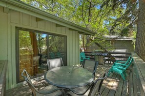 An outdoor patio with a round table and chairs, a grill, and a view of the surrounding trees. - Bear Ski Retreat by Destination Big Bear: Game Room! Cable TV! Close to Bear Mountain! Pet Friendly! (Big Bear Lake CA)