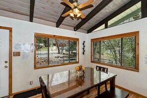 A dining area with a wooden table and chairs, large windows with blinds, a ceiling fan, and a door with a glass panel. - Bear Ski Retreat by Destination Big Bear: Game Room! Cable TV! Close to Bear Mountain! Pet Friendly! (Big Bear Lake CA)