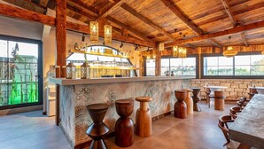 A rustic bar area with wooden beams, a bar counter with bottles, and wooden stools.