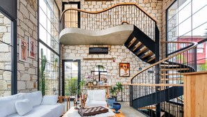 A modern interior with a stone wall, a white sofa, a wooden coffee table, and a spiral staircase.