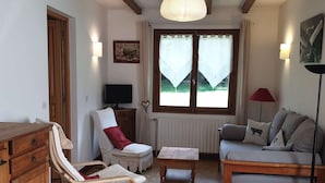 Un accogliente soggiorno con pavimento in legno, un divano, una poltrona, un tavolino, una TV e una finestra con tende.