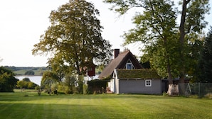 Et hus med stråtækt tag, omgivet af en velplejet græsplæne og træer.